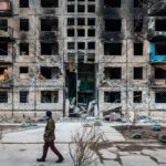 Seorang pria berjalan melewati blok apartemen yang dihantam rudal saat perang Rusia vs Ukraina (Gambar: Shutterstock, Maret 2022)