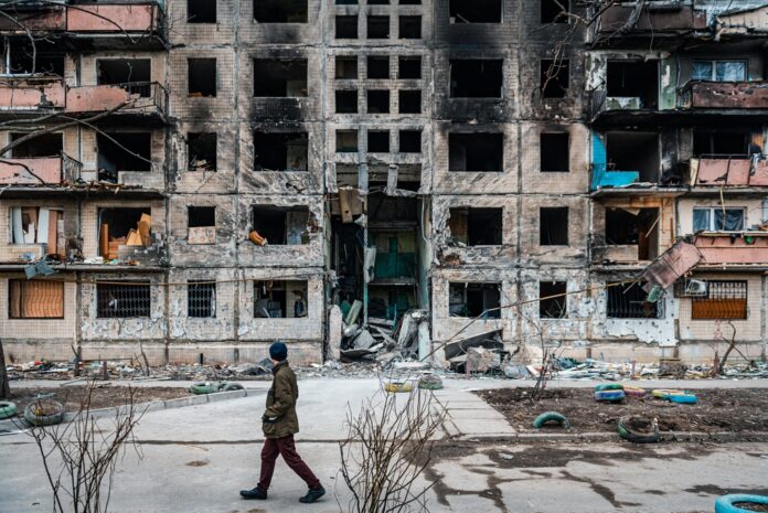 Seorang pria berjalan melewati blok apartemen yang dihantam rudal saat perang Rusia vs Ukraina (Gambar: Shutterstock, Maret 2022)